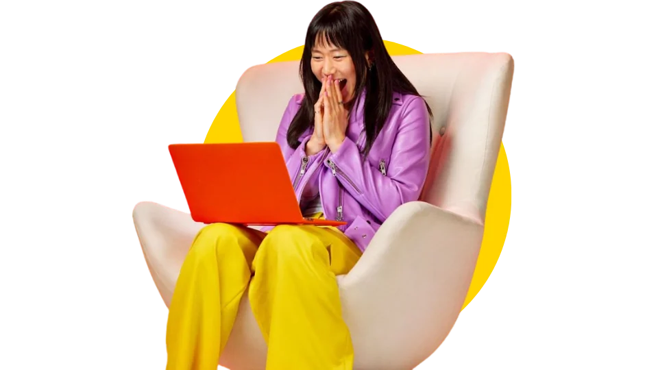 A woman in an armchair, delighted by what she sees on her laptop
